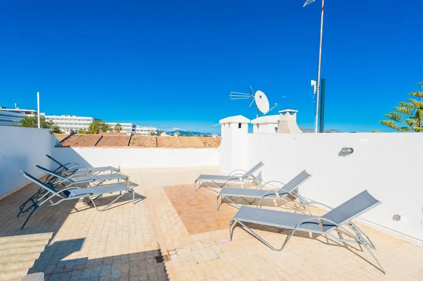 Una terraza soleada en la azotea con asientos reclinables y cielo azul despejado.