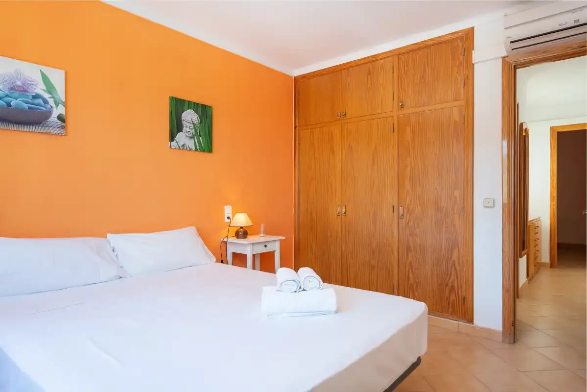 Un dormitorio con una cama blanca, una pared naranja y un armario de madera.