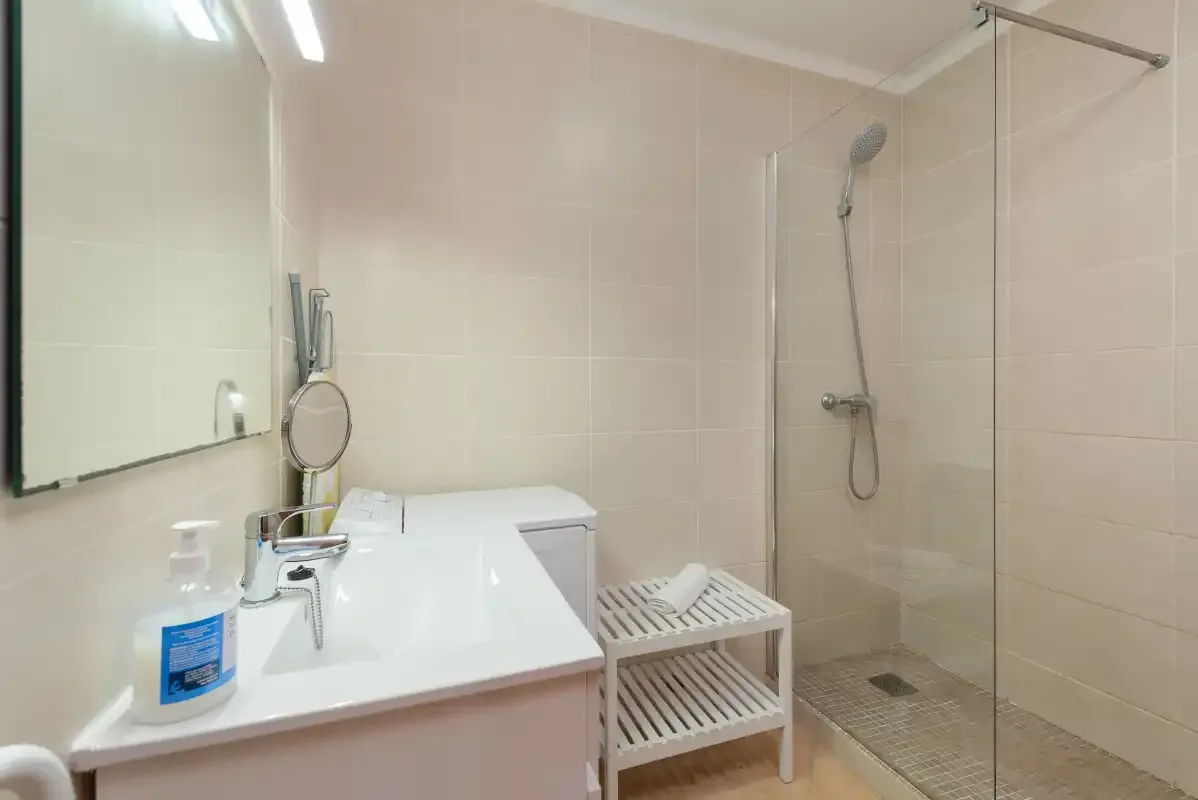 Un baño alicatado con lavabo, espejo y ducha de vidrio.