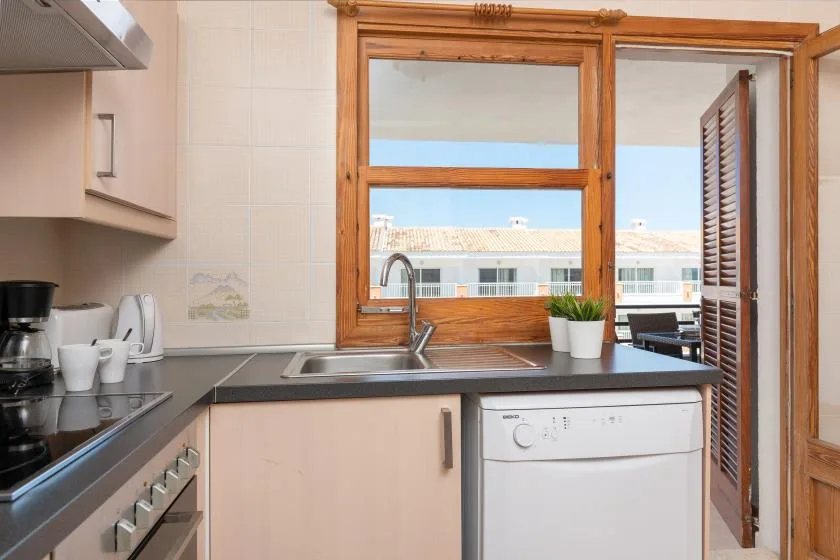 Una cocina con fregadero y lavavajillas debajo de una ventana amplia.