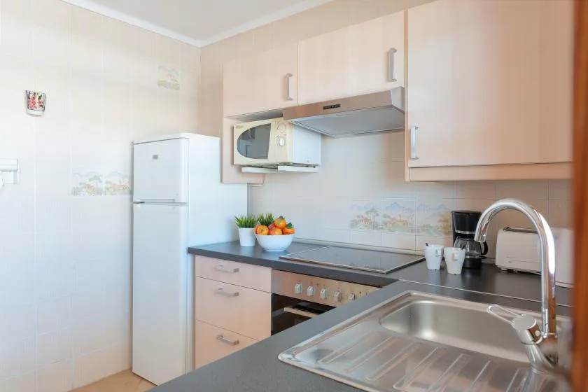 Una cocina luminosa con gabinetes claros, un refrigerador y un fregadero.