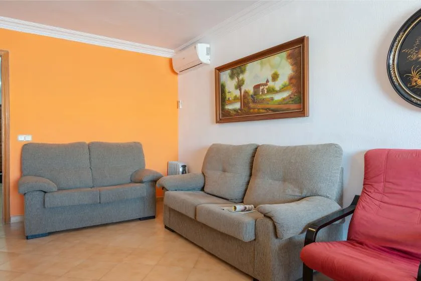 Una sala de estar con asientos grises, una pared naranja y cuadros enmarcados.