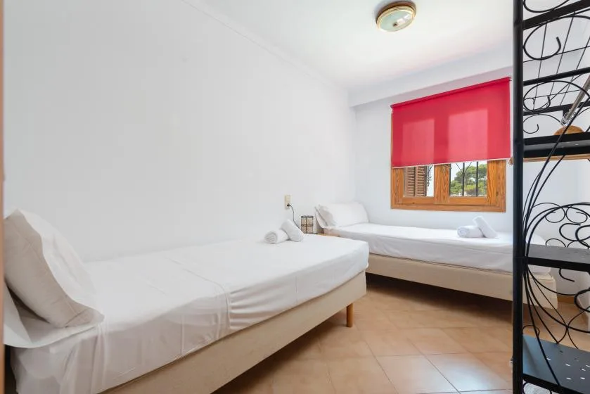 Un dormitorio luminoso con dos camas y una persiana roja.