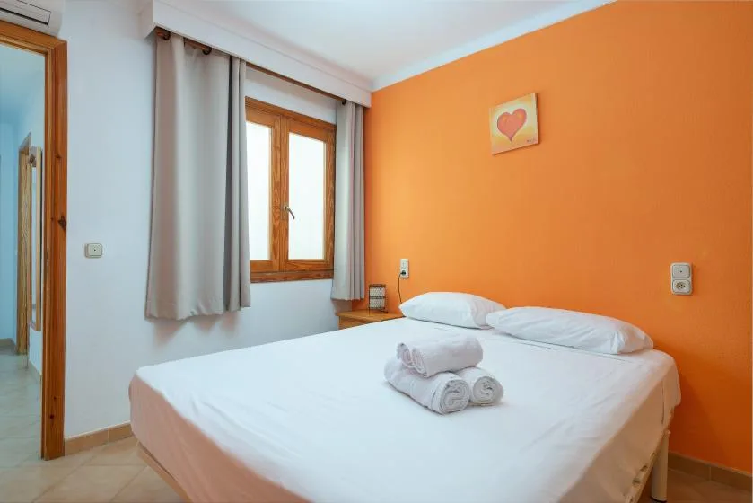 Un dormitorio con una cama doble, toallas dobladas y una pared naranja.