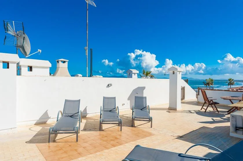 Una terraza soleada en la azotea con asientos, paredes blancas y vistas al mar.