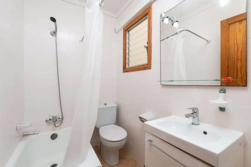 Un baño con bañera, inodoro y lavabo bajo un espejo de pared.