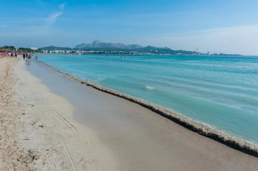 Una playa de arena bordea aguas turquesas, con montañas lejanas en el horizonte.