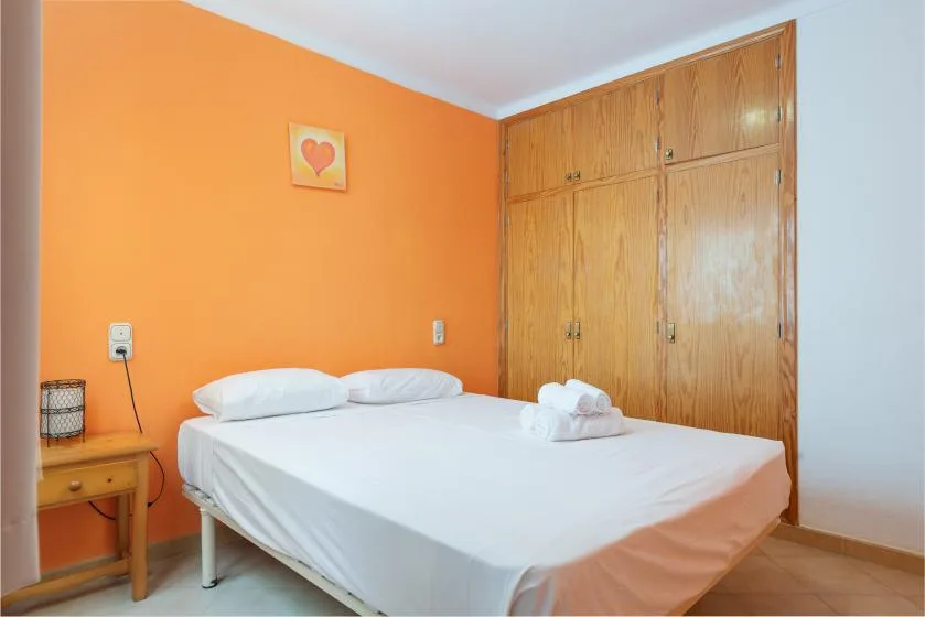 Un dormitorio con una cama blanca, una pared naranja y armarios empotrados de madera.