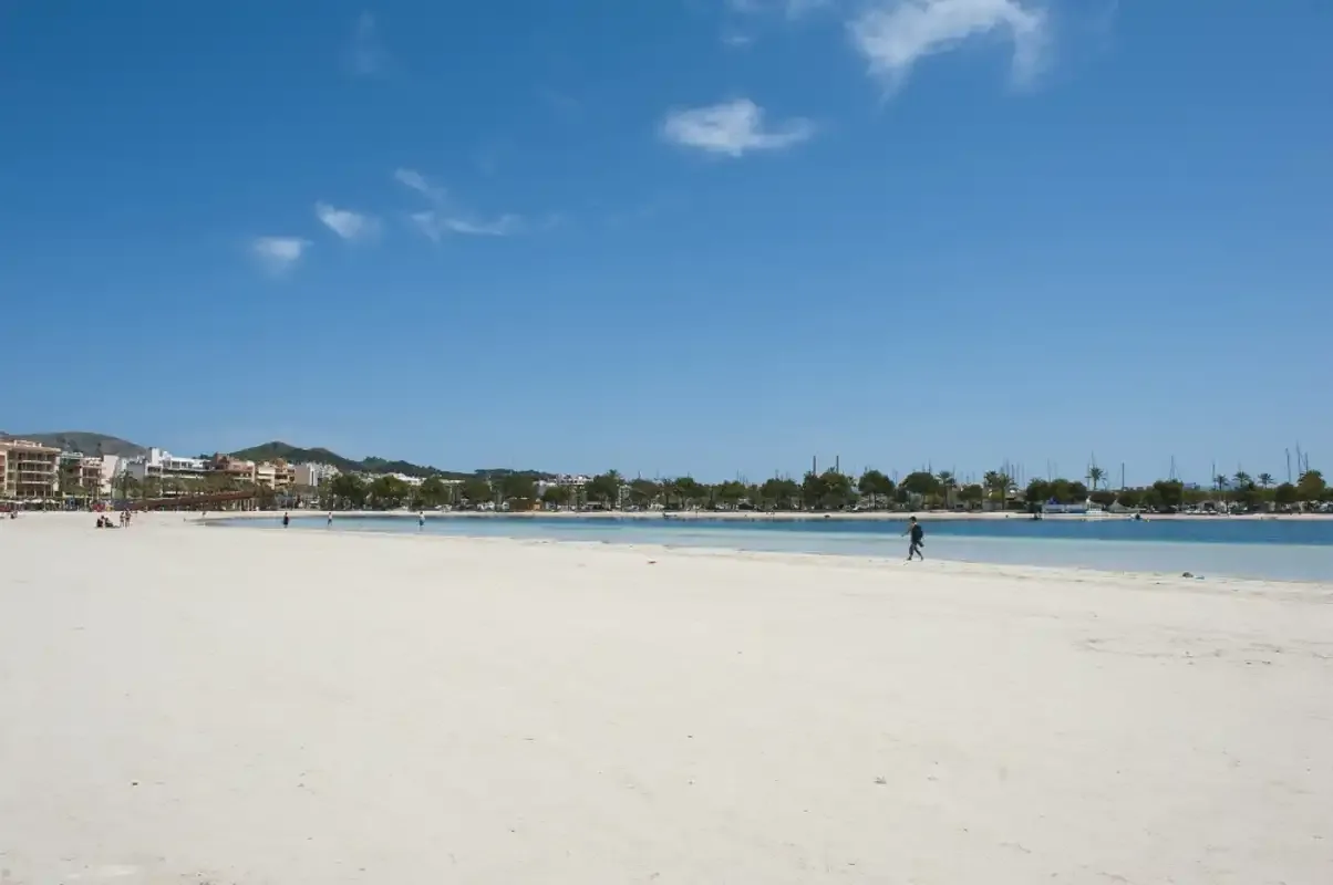 Una amplia playa de arena se extiende junto a aguas azules tranquilas bajo un cielo despejado.