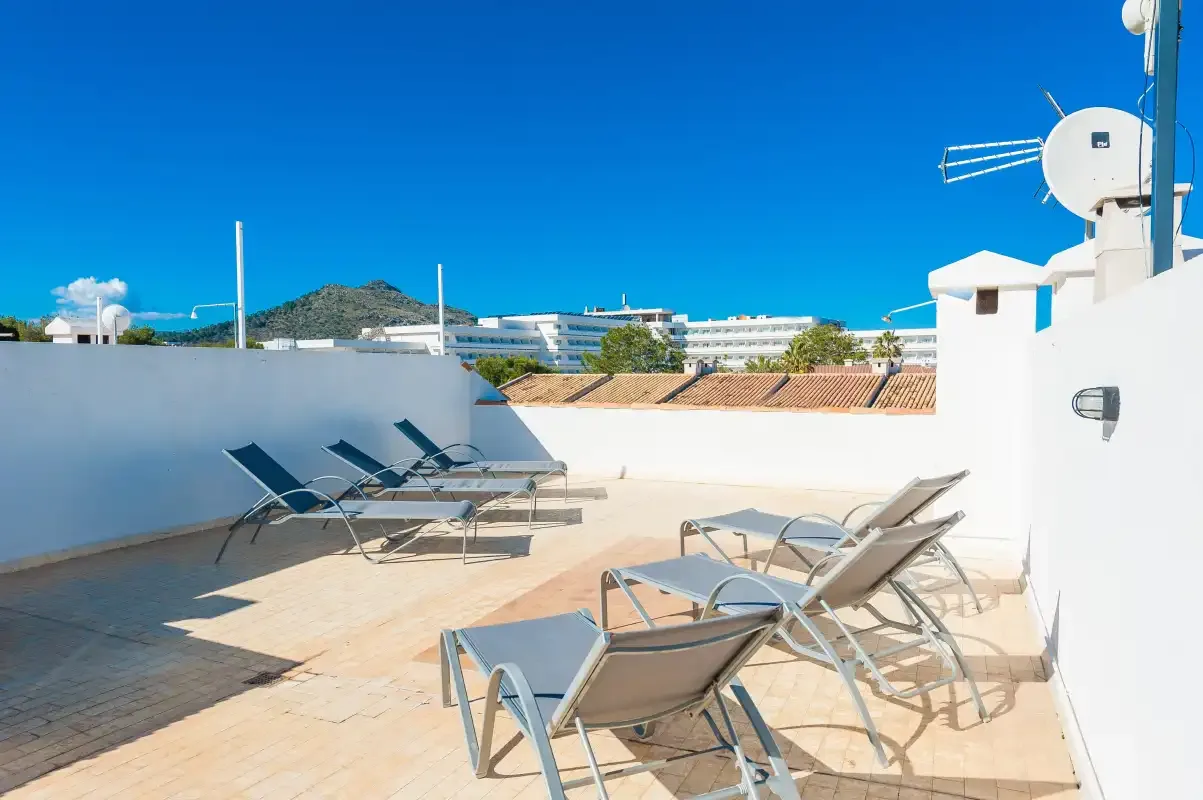 Una terraza soleada en la azotea tiene asientos reclinables y vistas a edificios cercanos.