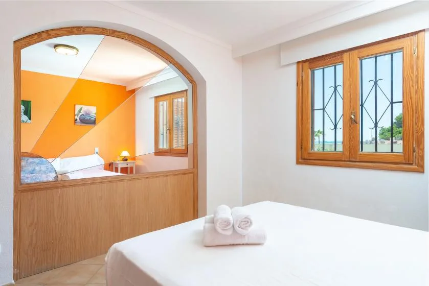 Un dormitorio con una cama blanca en primer plano y un arco que da a otra habitación.