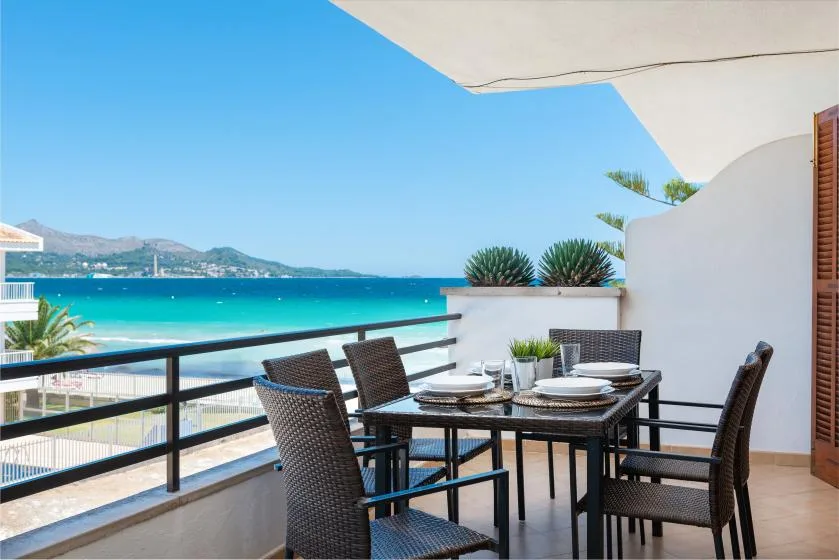 Una terraza junto al mar tiene una mesa con sillas y vistas al agua azul.