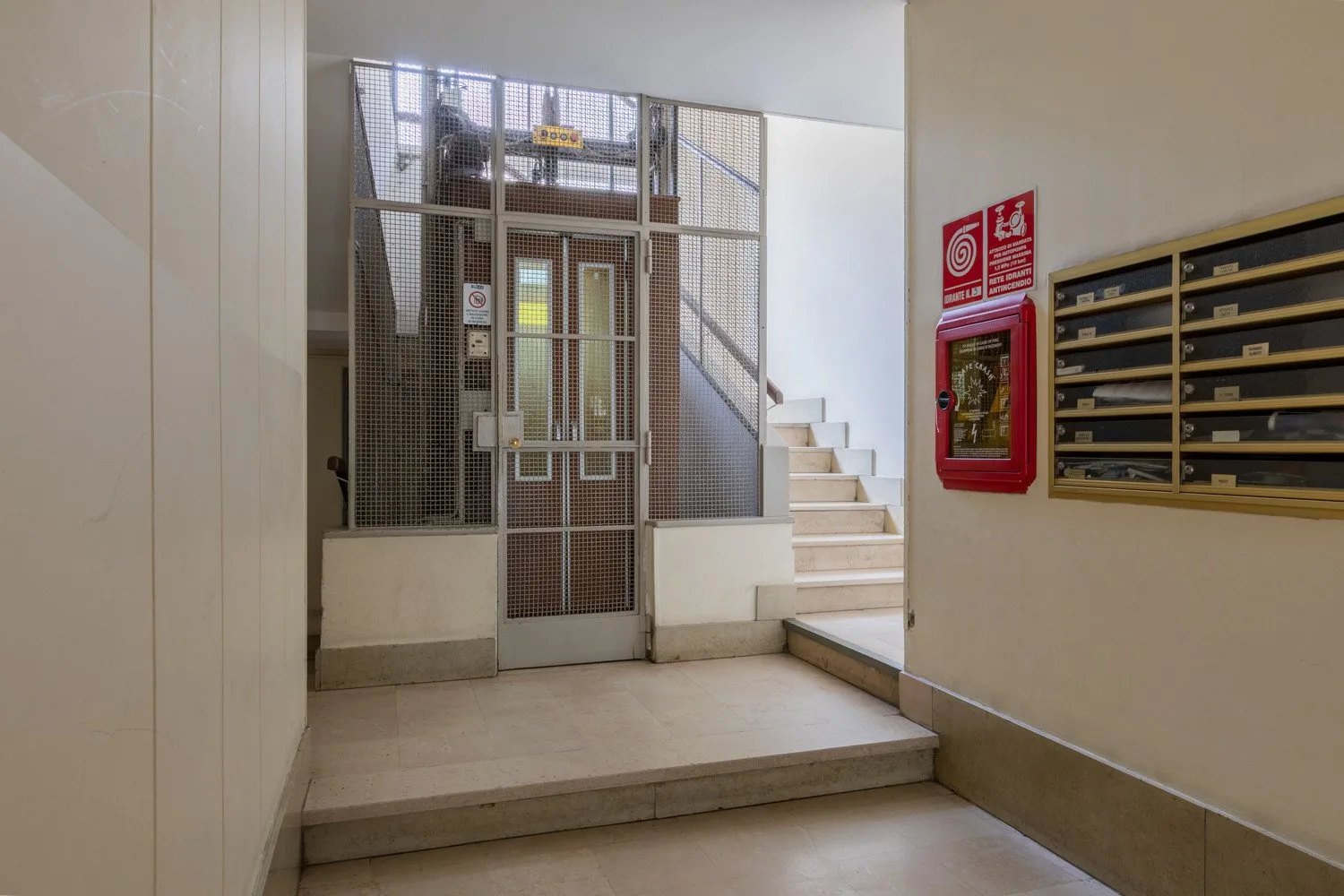 Un pasillo de edificio con un ascensor enrejado y una escalera.