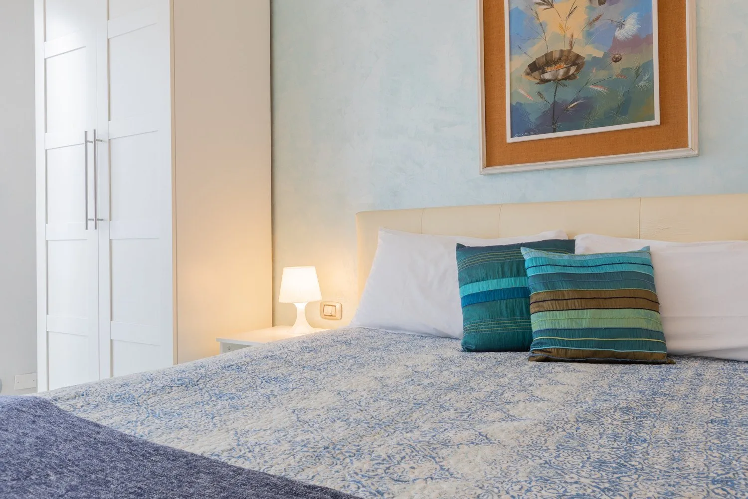 Un dormitorio con una cama bien tendida y almohadas de rayas coloridas.