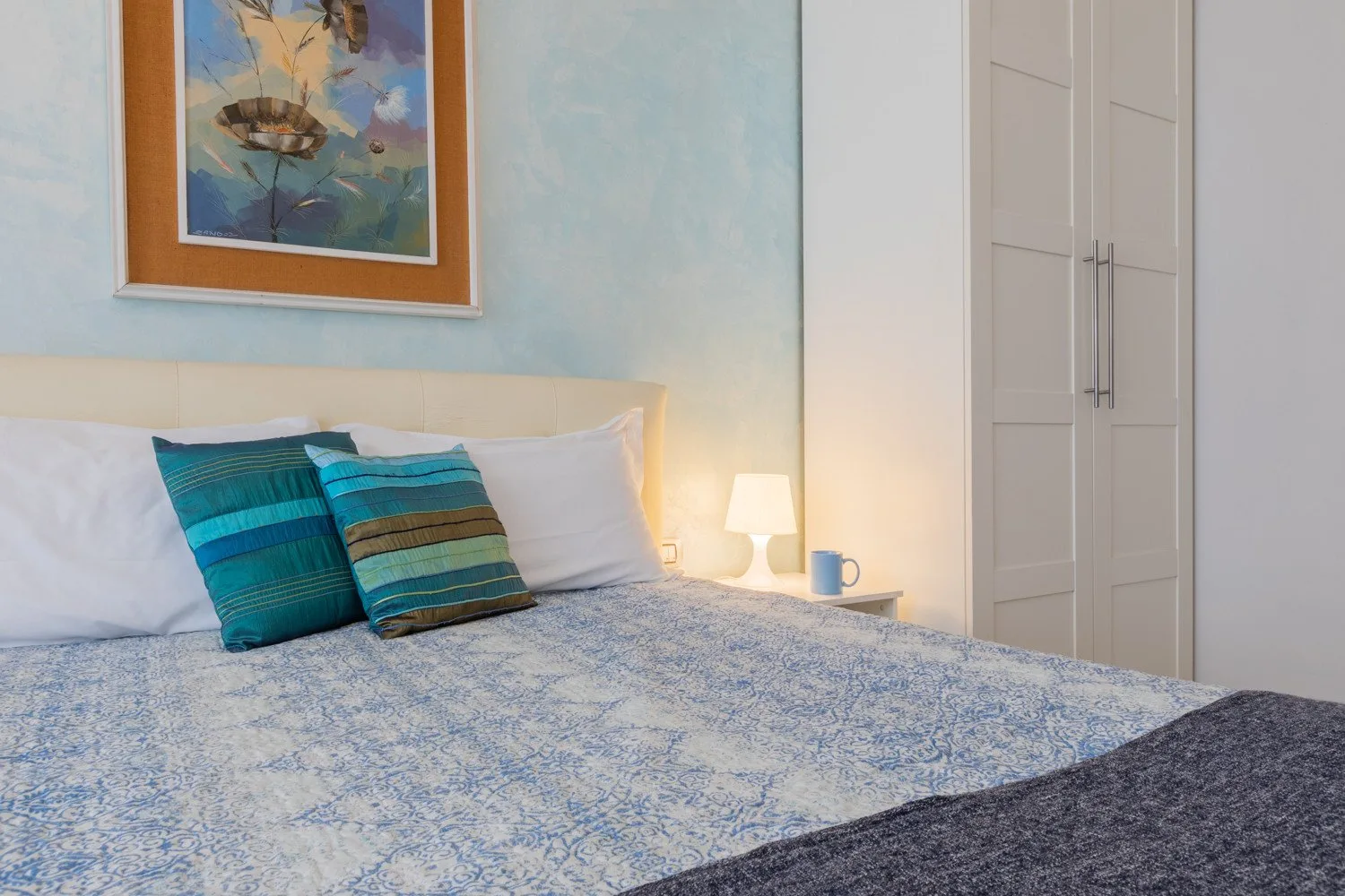 Un dormitorio con una cama, cojines de colores y un cuadro enmarcado en la pared.