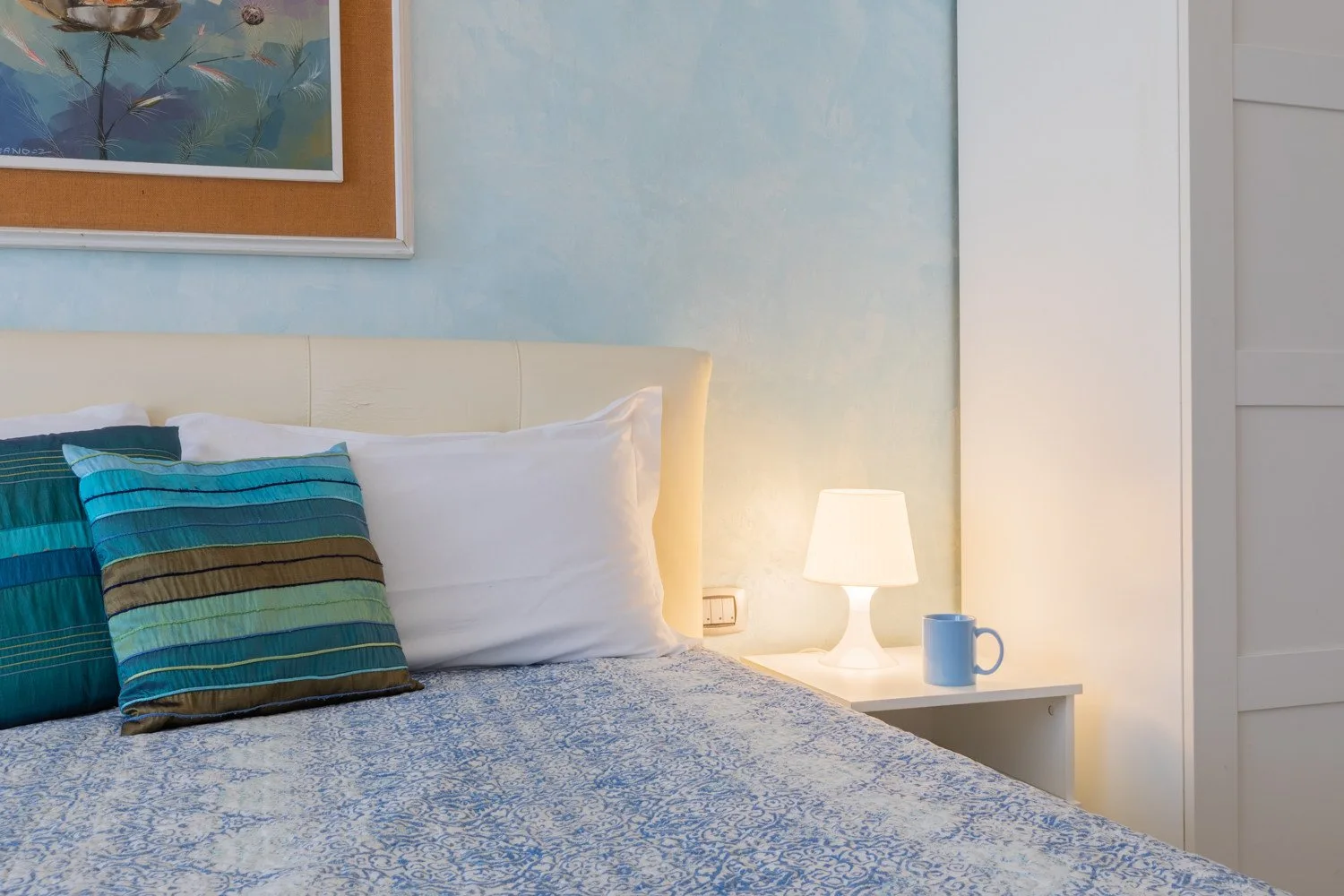Un dormitorio con una cama, ropa de cama estampada y una mesita con una lámpara.