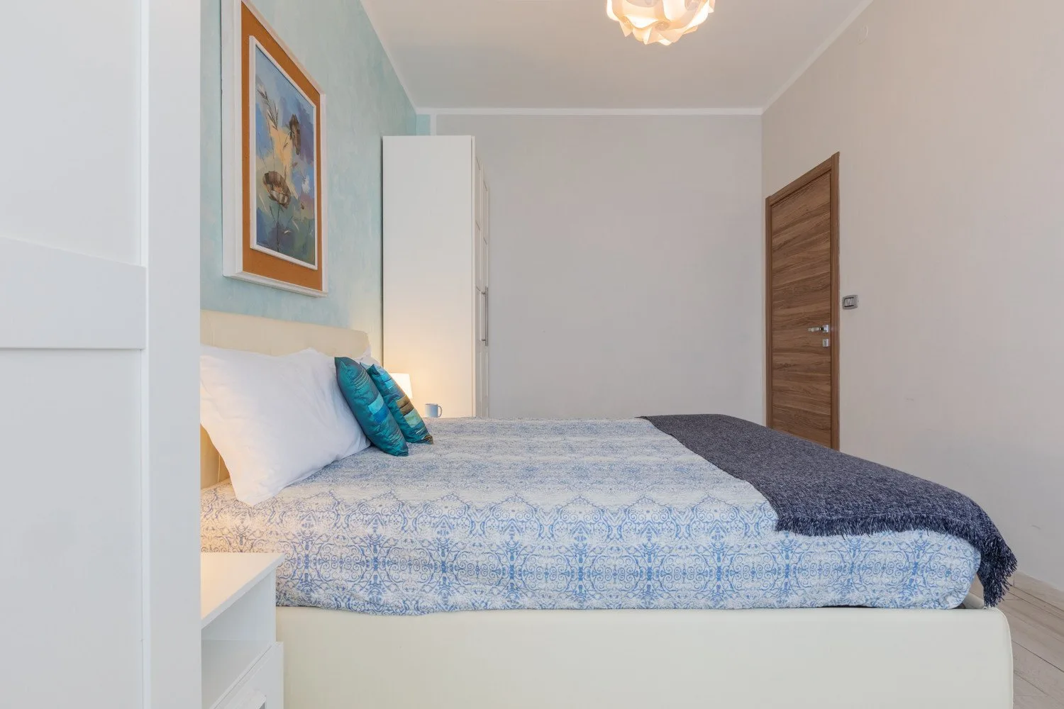 Un dormitorio con una cama cubierta con ropa de cama azul estampada y arte enmarcado en la pared.