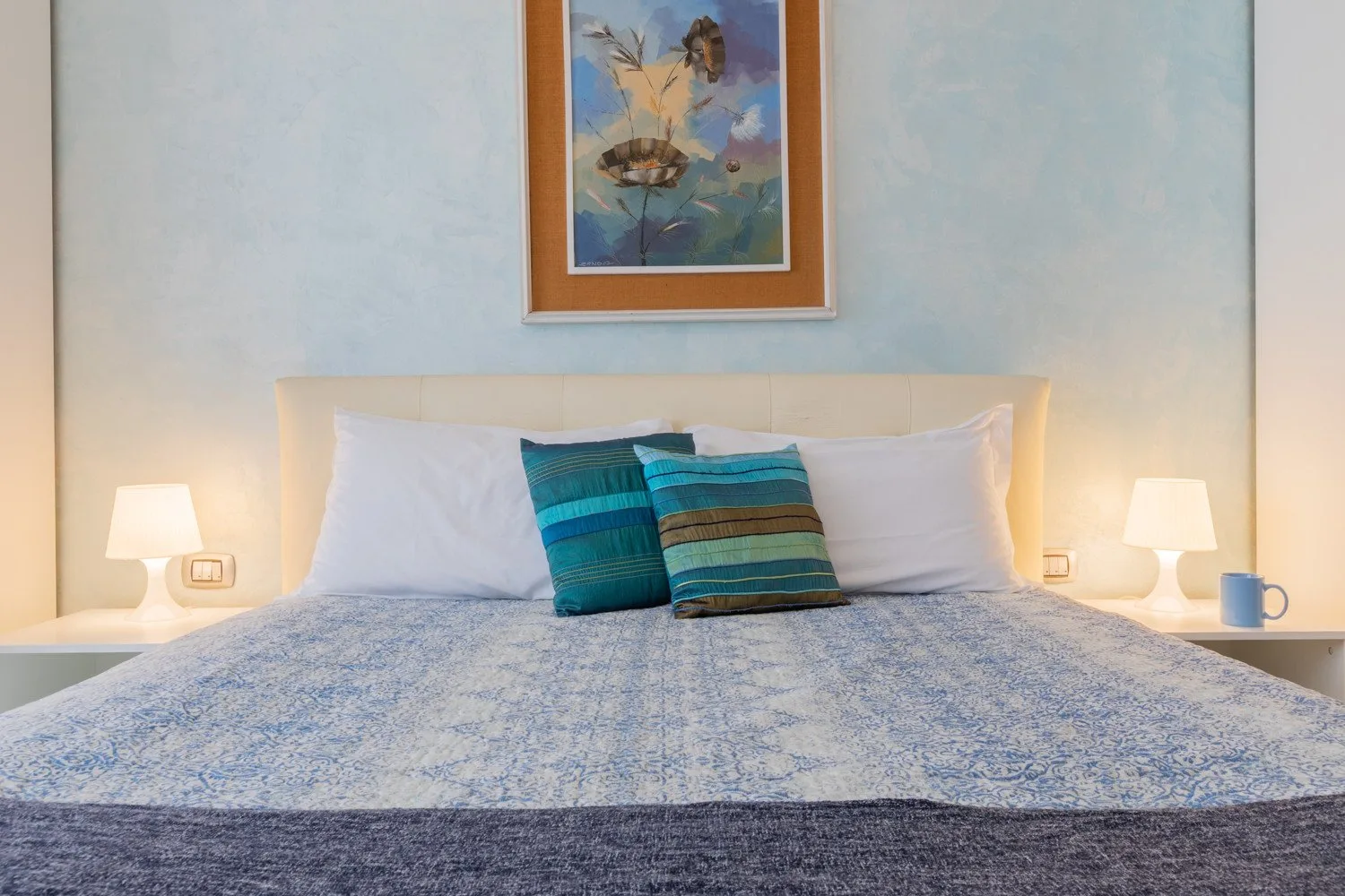 Un dormitorio con una cama bien tendida, cojines a rayas y lámparas de noche.