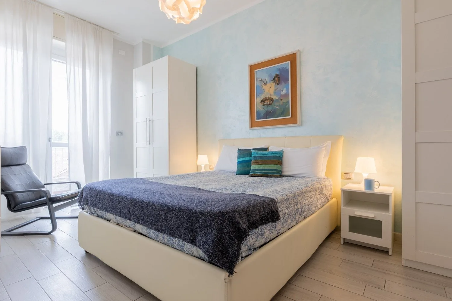 Un dormitorio con una cama grande, mesillas de noche y una silla junto a la ventana.