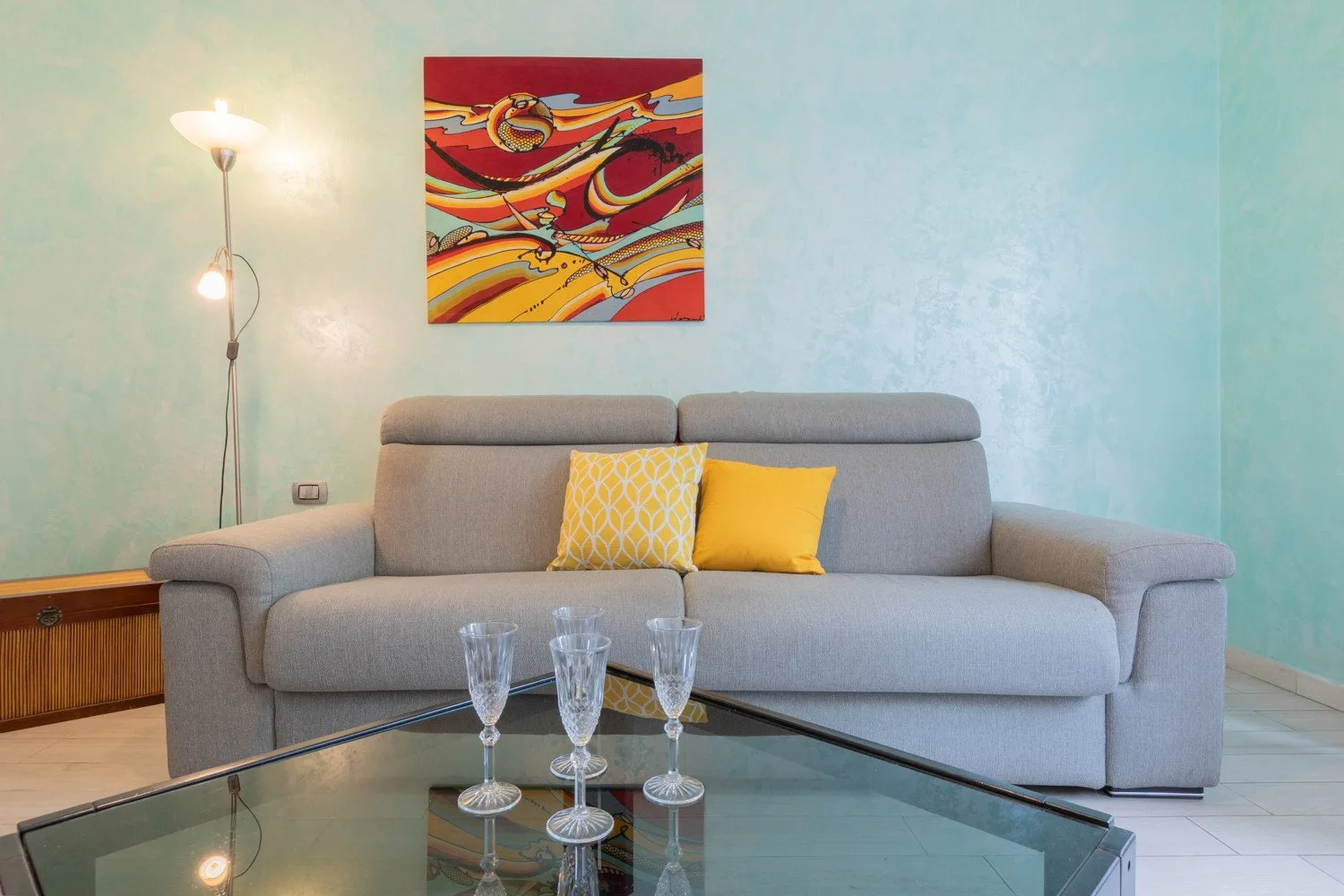 Una sala de estar con un sofá gris, cojines coloridos y una mesa de centro de vidrio.