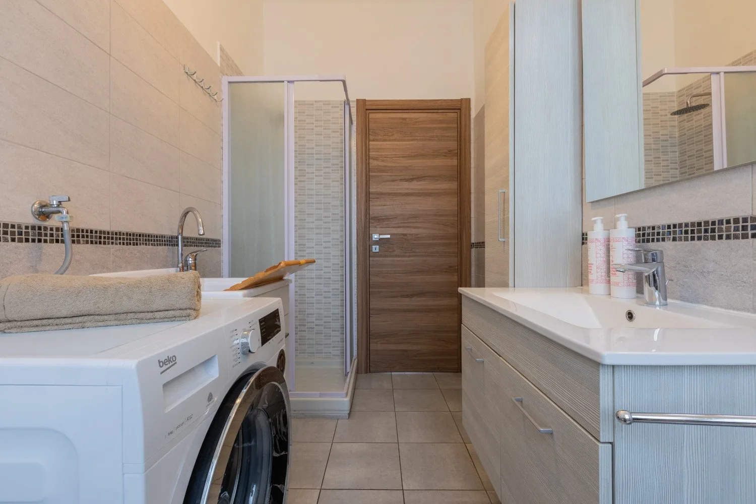 Un baño con lavadora, lavabo y una ducha con mampara de vidrio.