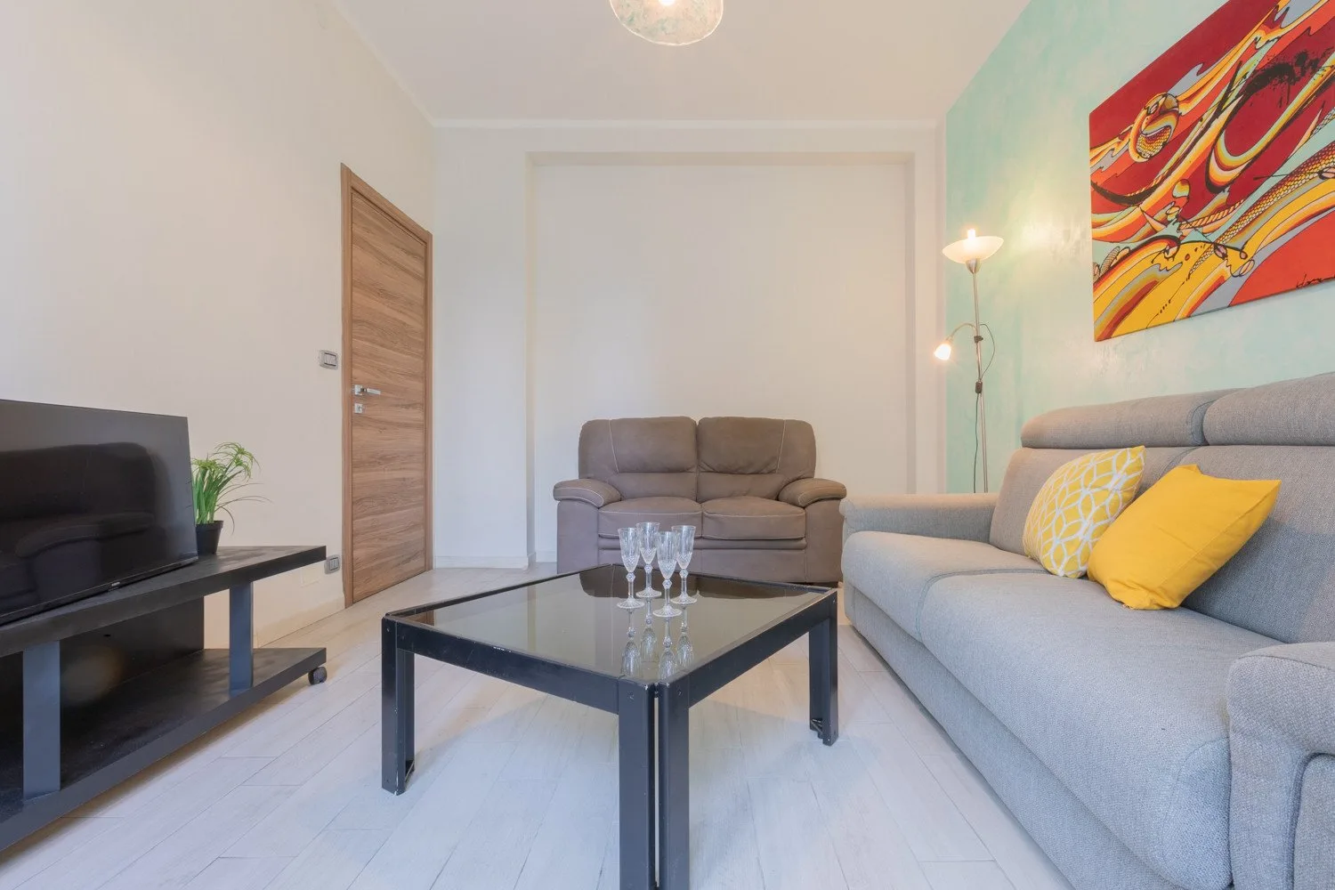 Una sala de estar con asientos alrededor de una mesa de centro de vidrio y arte colorido en la pared.