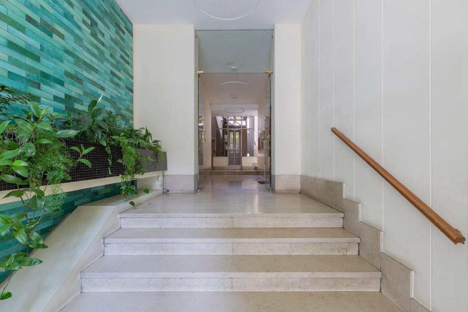 Una escalera de azulejos con pasamanos de madera conduce a una entrada de vidrio.