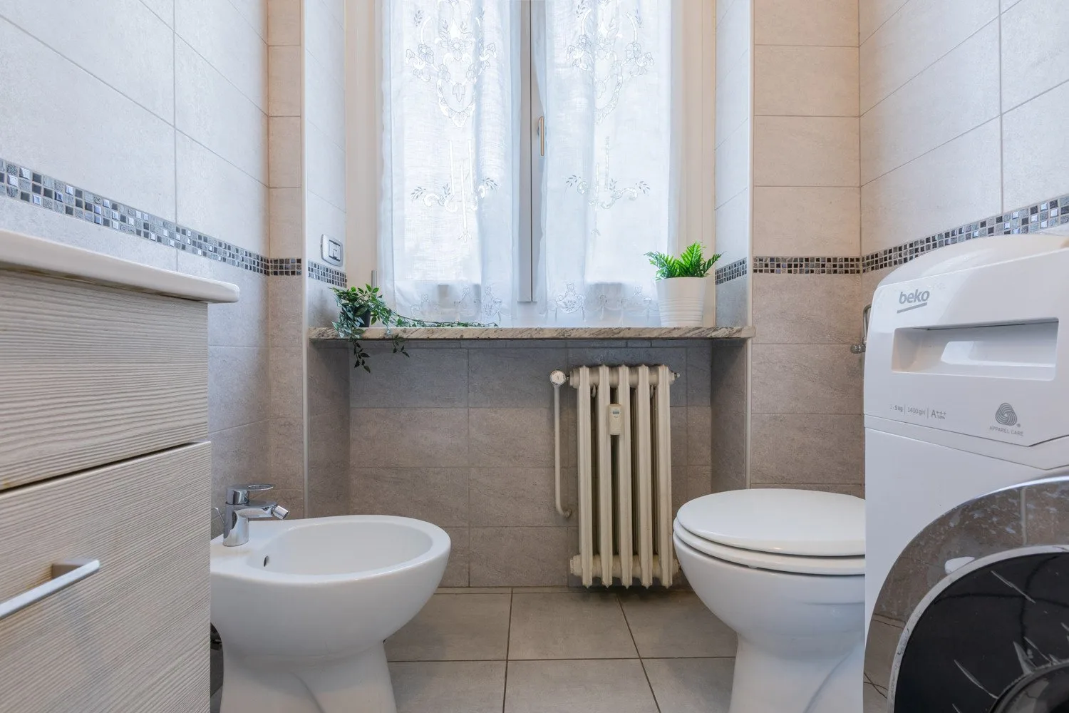 Un baño alicatado con ventana, bidé, inodoro y lavadora.