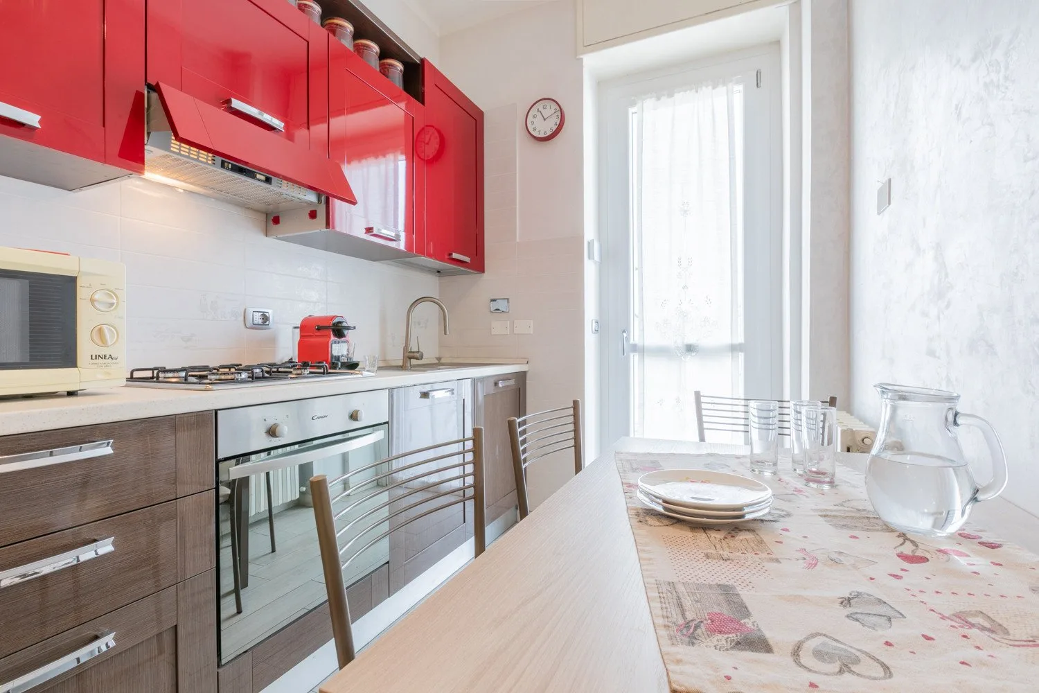 Una cocina luminosa con comedor, gabinetes rojos y una mesa junto a la ventana.