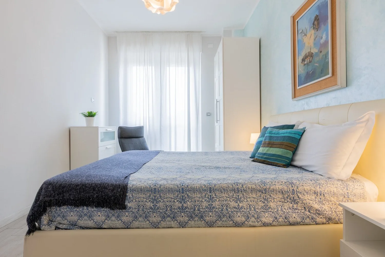 Un dormitorio luminoso con una cama bien tendida y cortinas translúcidas.