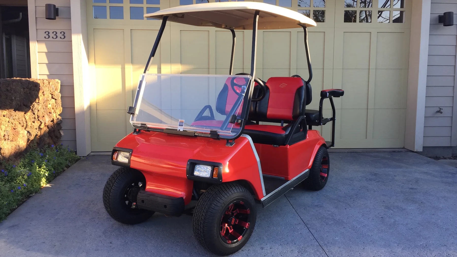 Un carrito de golf rojo está estacionado frente a un garaje.