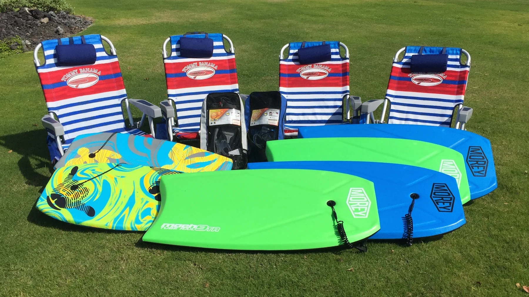 Sillas de playa y tablas de bodyboard coloridas están dispuestas sobre el césped.