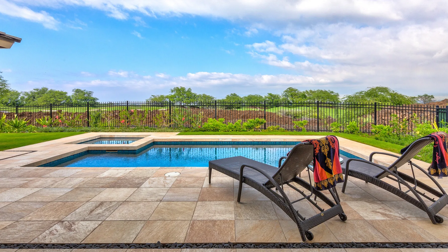 Una piscina exterior junto a un patio pavimentado con asientos reclinables.