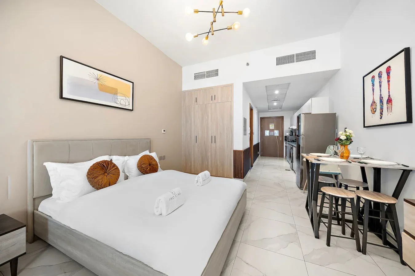Un dormitorio con una cama bien tendida junto a una mesa de comedor y una cocina pequeña.