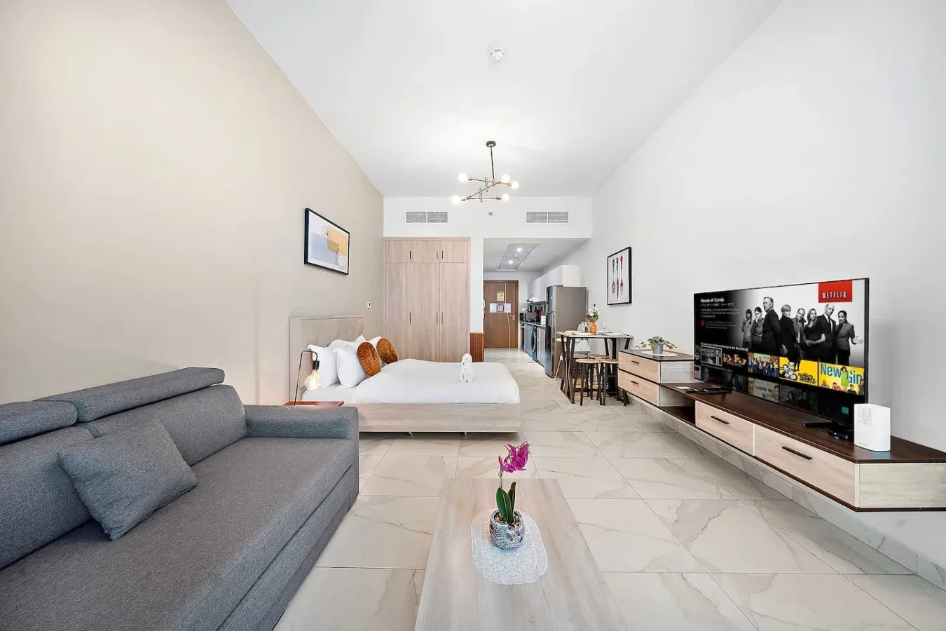 Una luminosa sala de estar con sofá gris, cama y televisor junto a la pared.