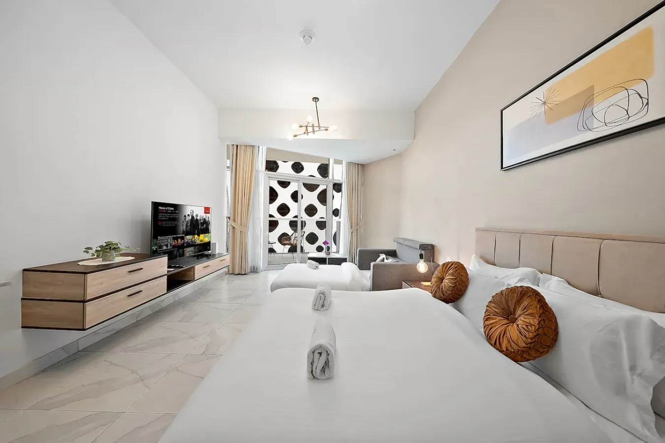 Un dormitorio luminoso con una cama grande, asientos junto a la cama y un televisor sobre un mueble bajo.