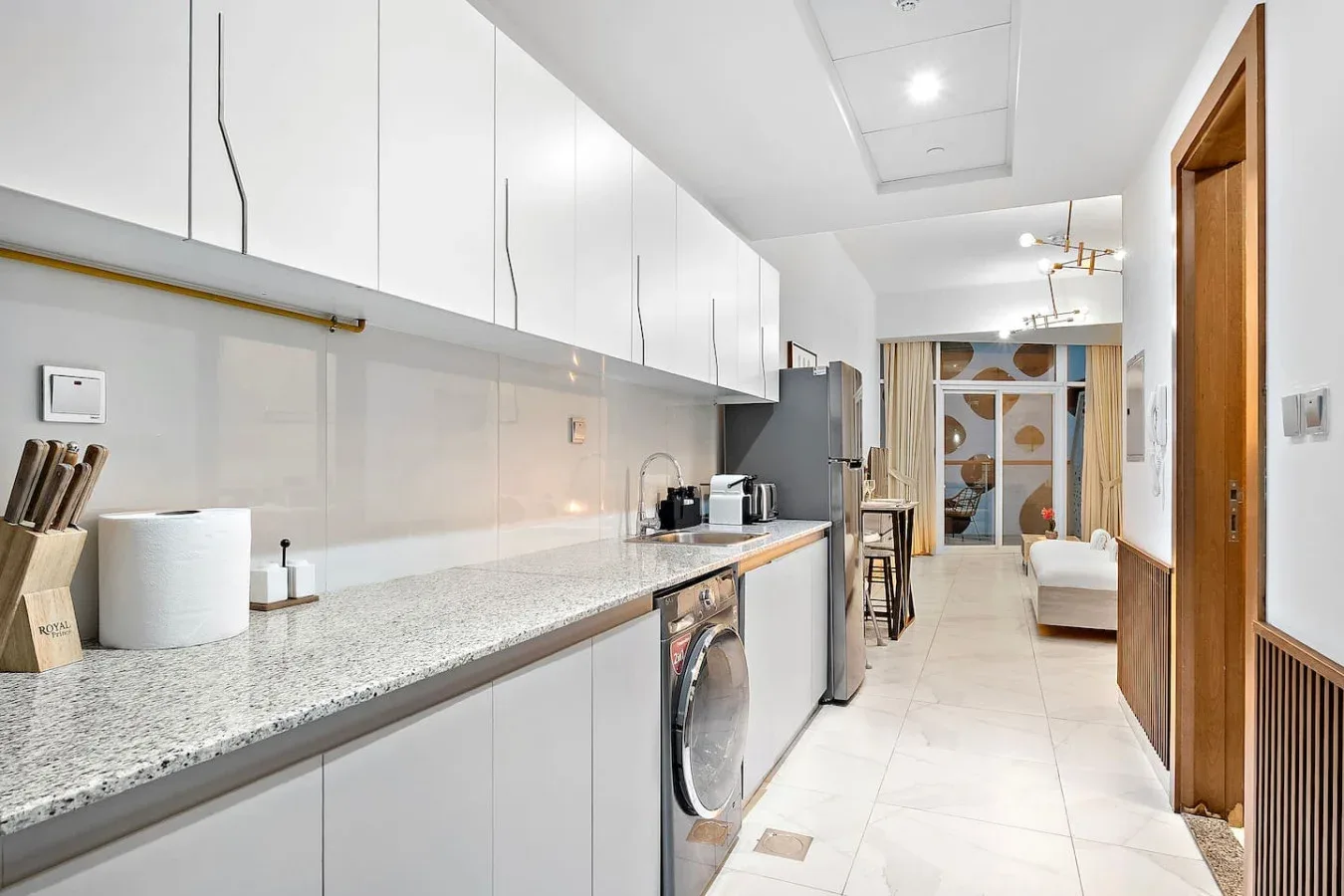 Una cocina luminosa con una encimera larga y electrodomésticos de lavandería, abierta a una sala de estar.