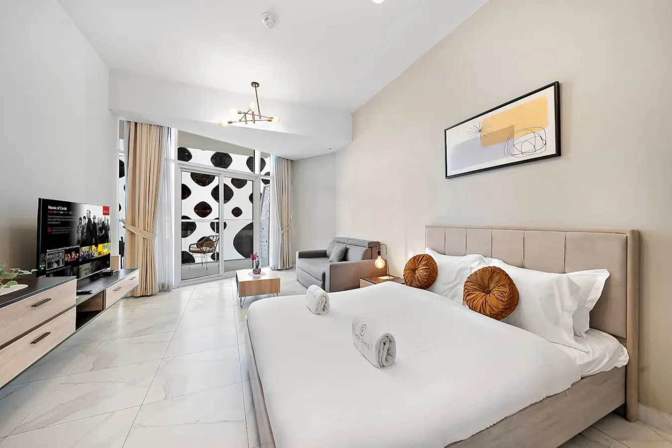 Un dormitorio luminoso con una cama grande, una zona de estar y ventanas al fondo.