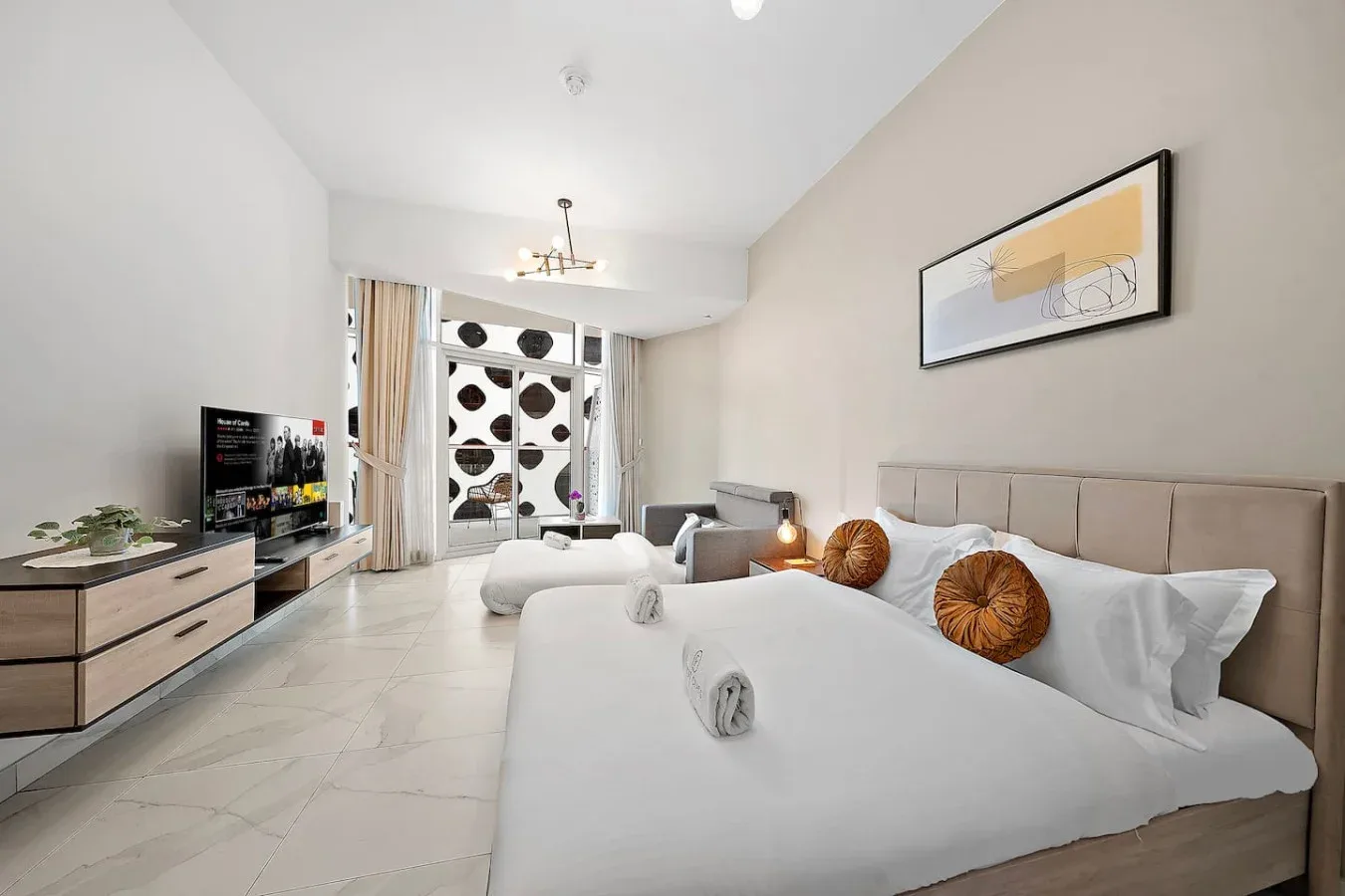 Un dormitorio luminoso con dos camas, un televisor y grandes ventanas estampadas.