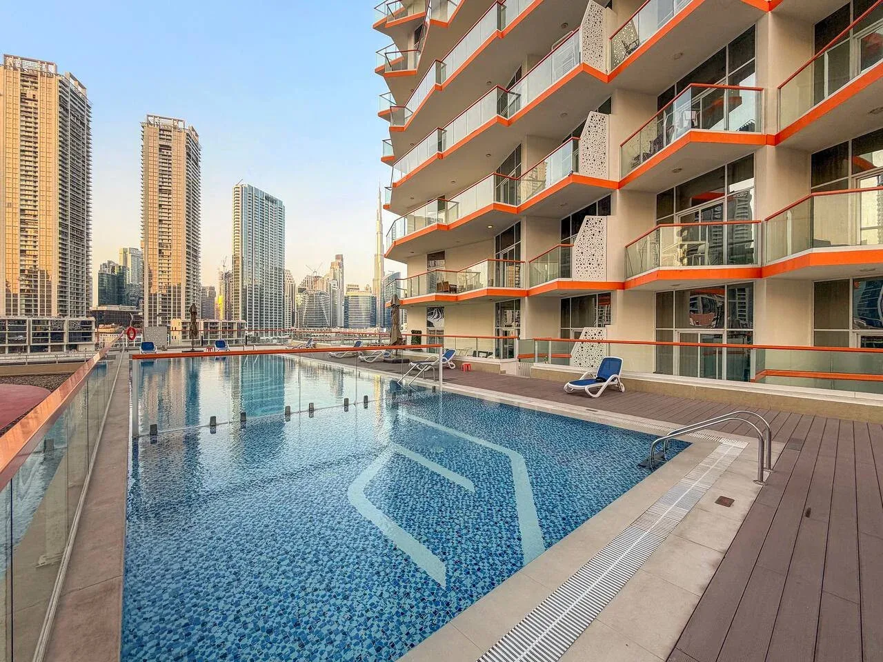 Una piscina al aire libre junto a un edificio moderno, con torres de la ciudad al fondo.