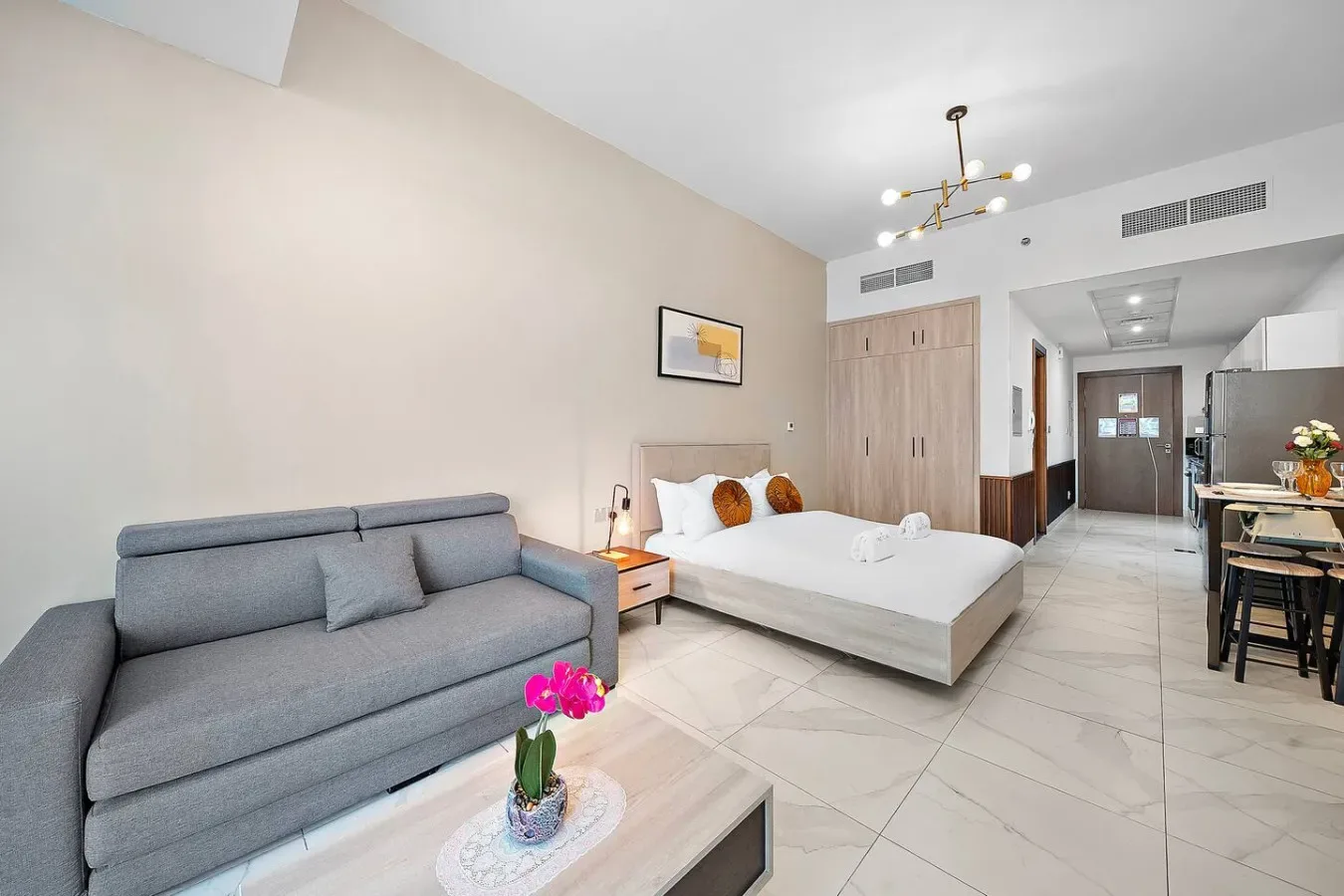Un dormitorio luminoso con una cama, asientos grises y una pequeña zona de comedor.
