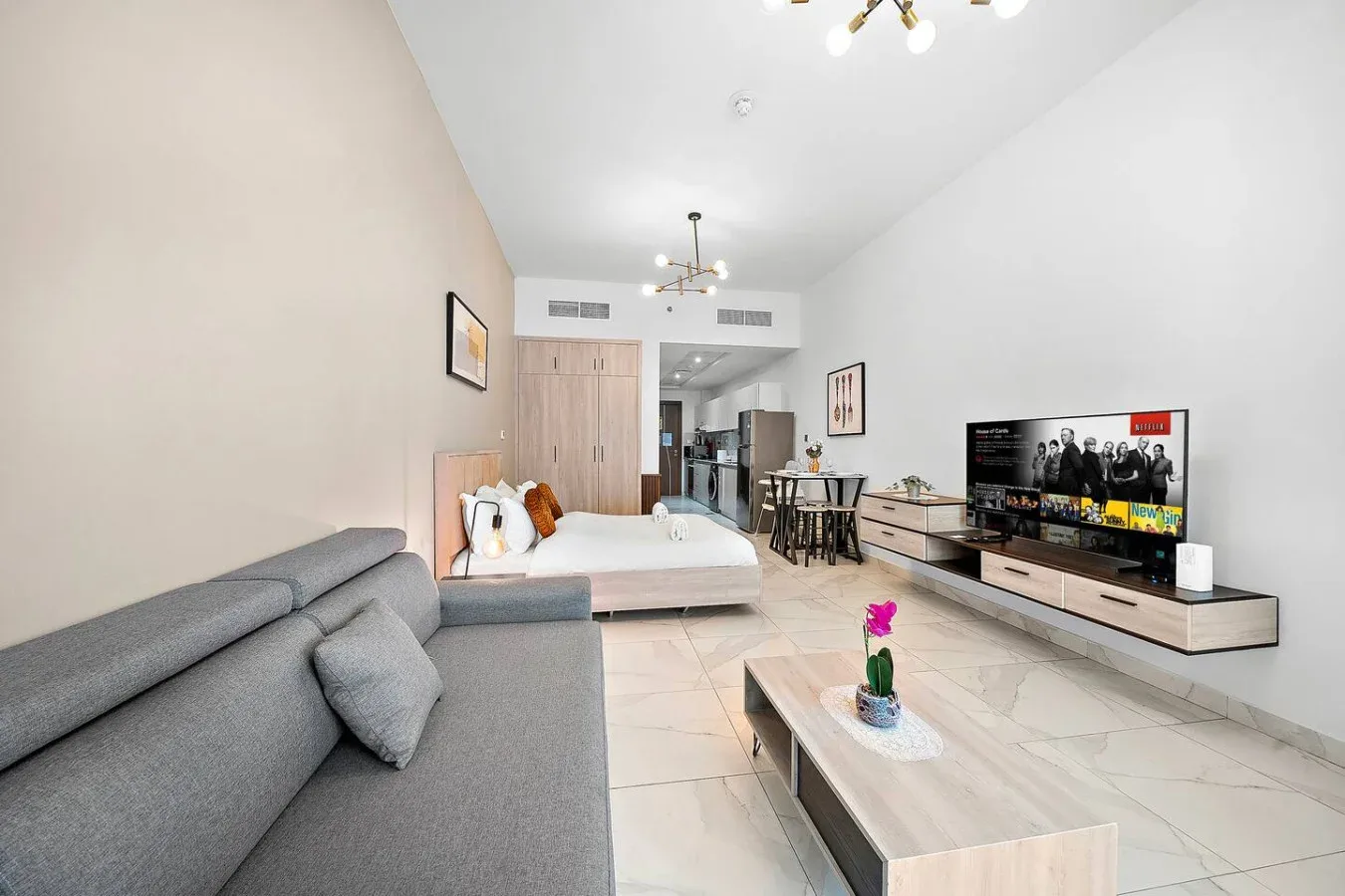 Una luminosa sala de estar diáfana con sofá gris, cama y televisor.