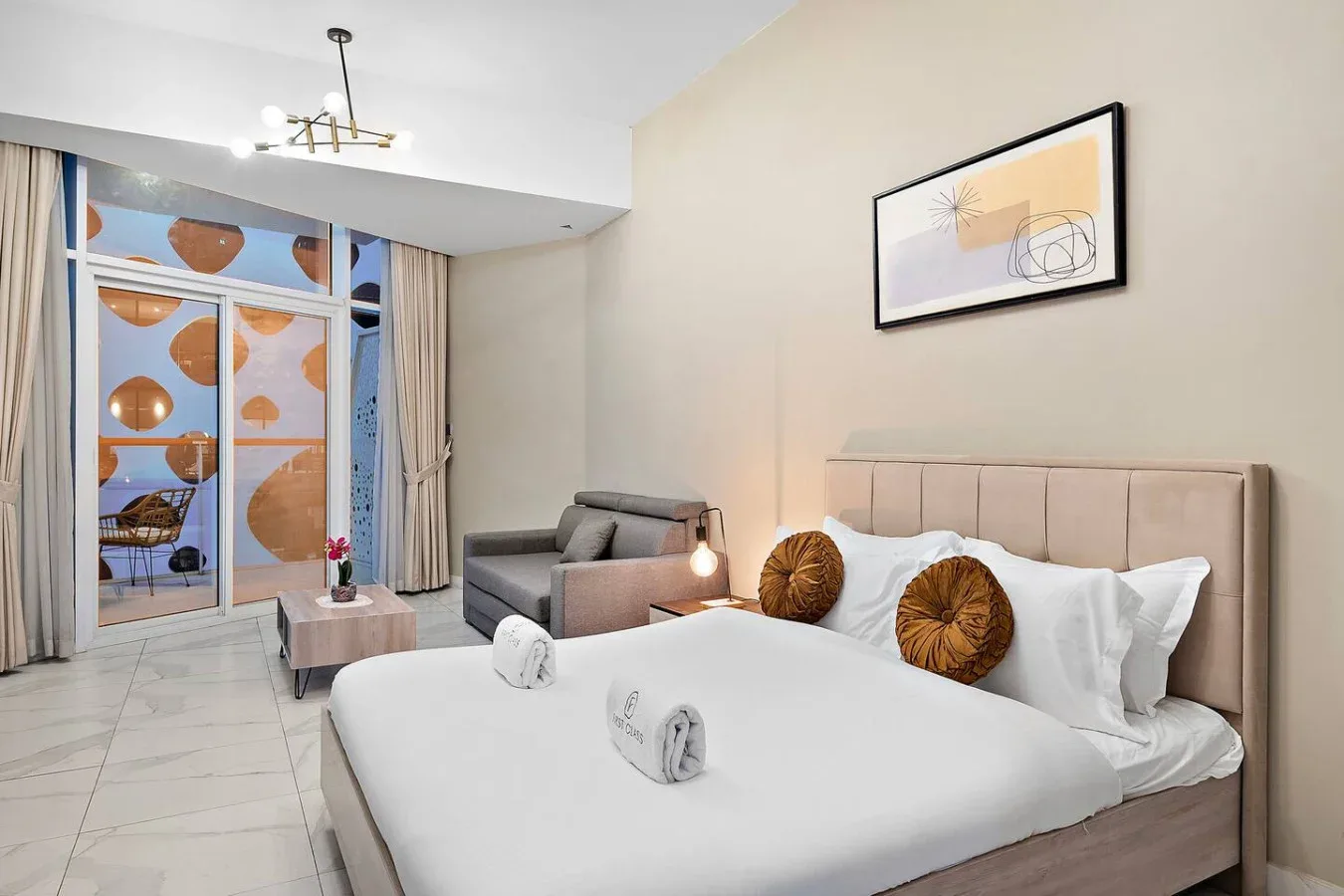 Un dormitorio con una cama tendida y una zona de asientos gris junto a las ventanas.