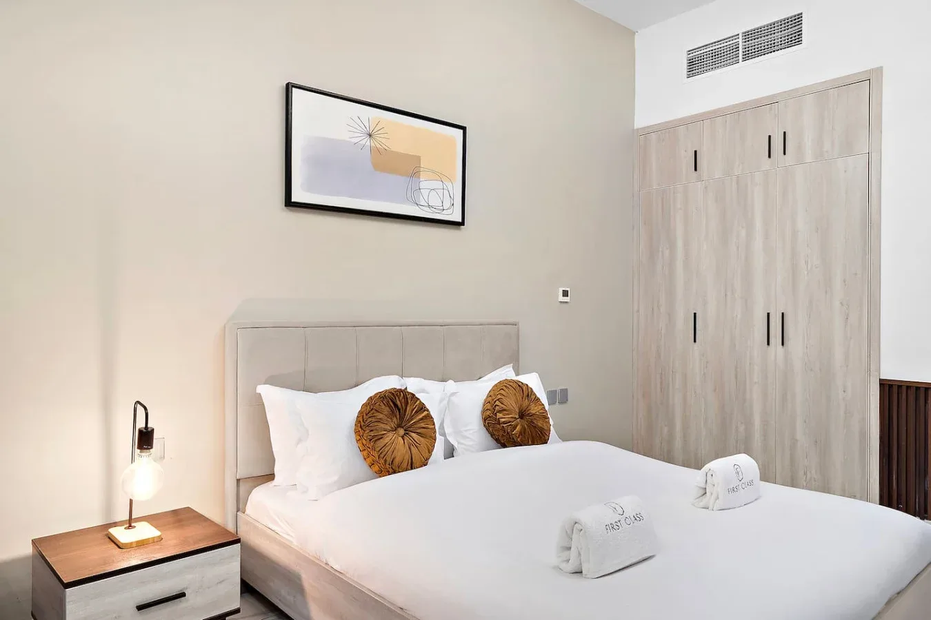 Un dormitorio con una cama tendida, cojines decorativos y un armario.