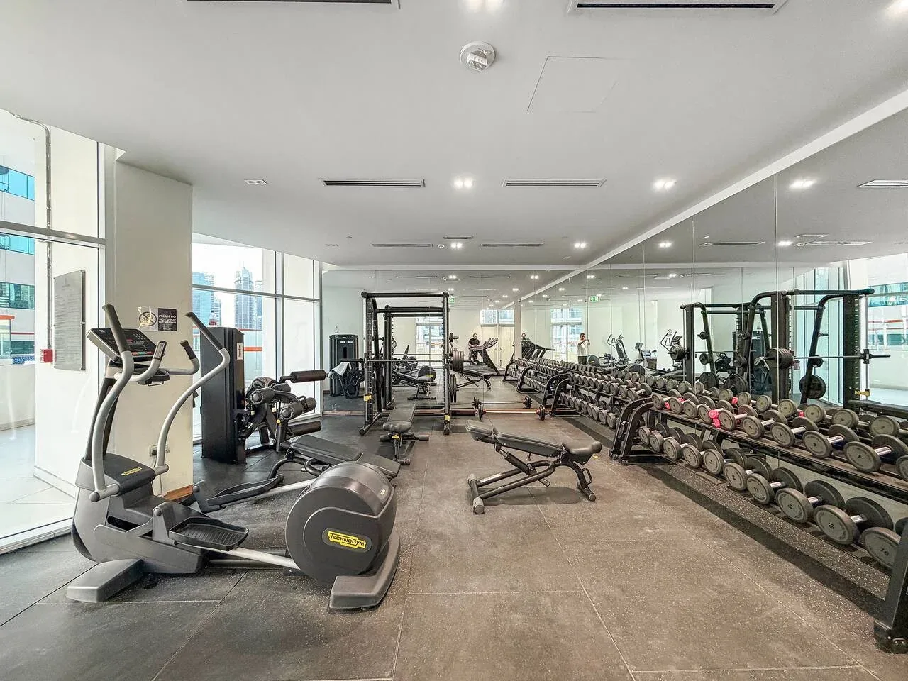 Un gimnasio con máquinas de ejercicio y pesas junto a paredes con espejos.