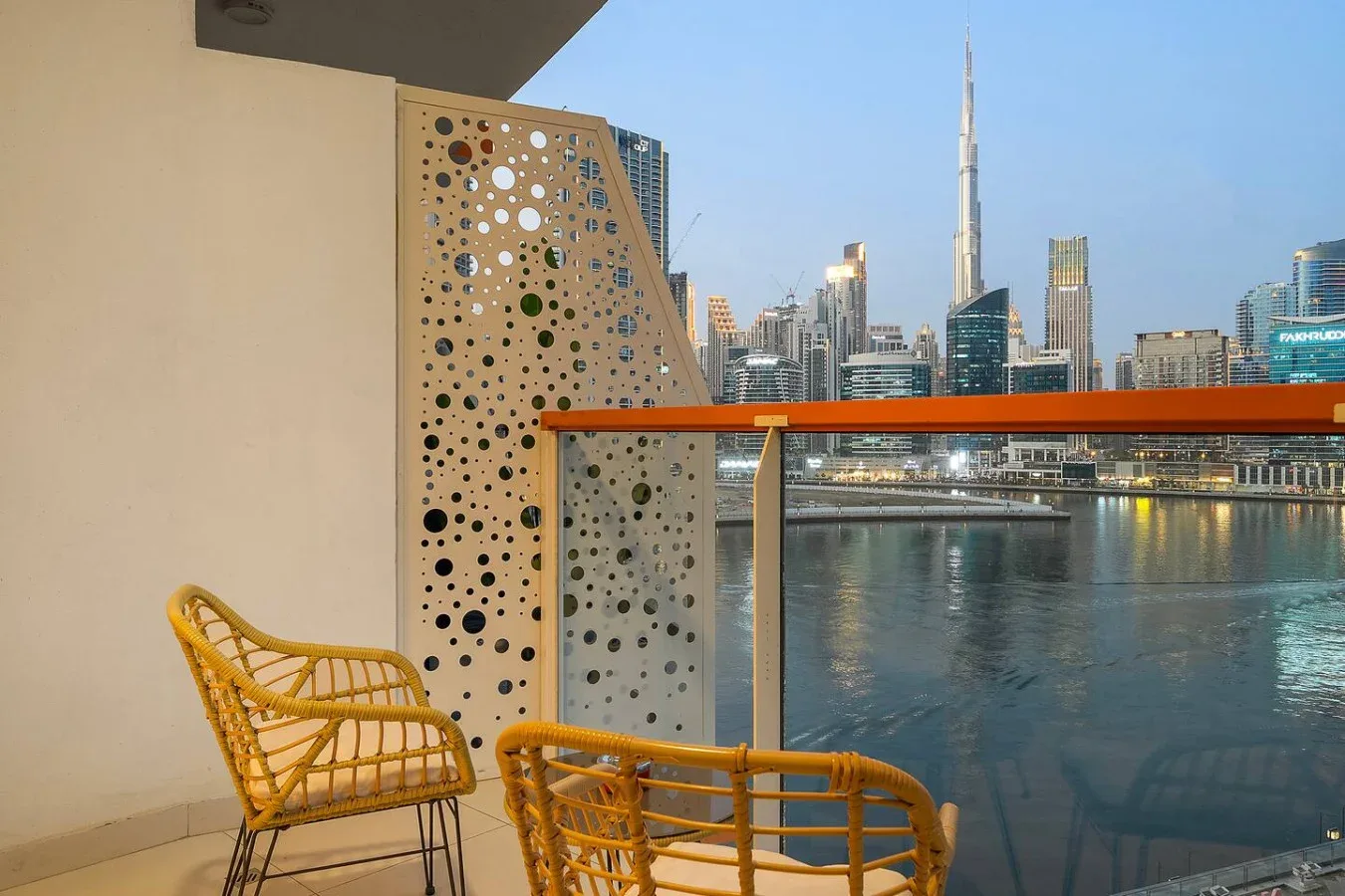 Un balcón con asientos tejidos da a un horizonte urbano junto al agua y una torre alta.