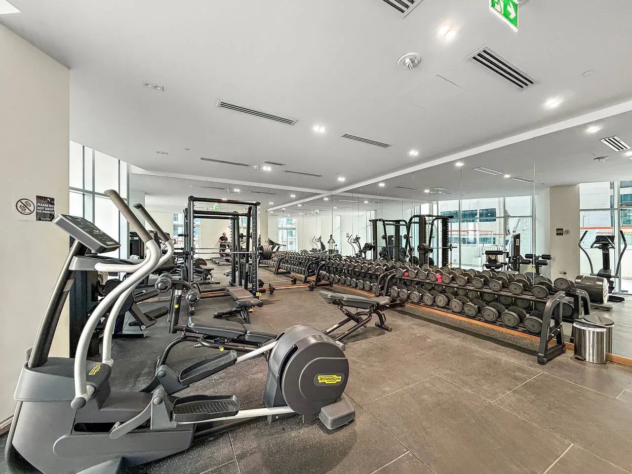 Un gimnasio con máquinas de ejercicio y un largo estante de mancuernas.