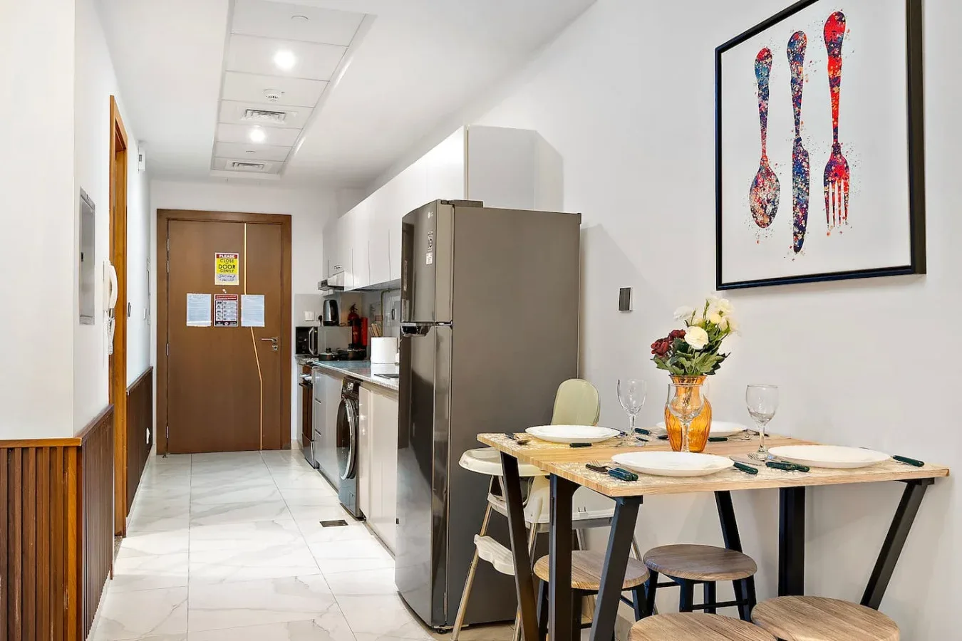 Una mesa está preparada junto a una cocina compacta con refrigerador y armarios.