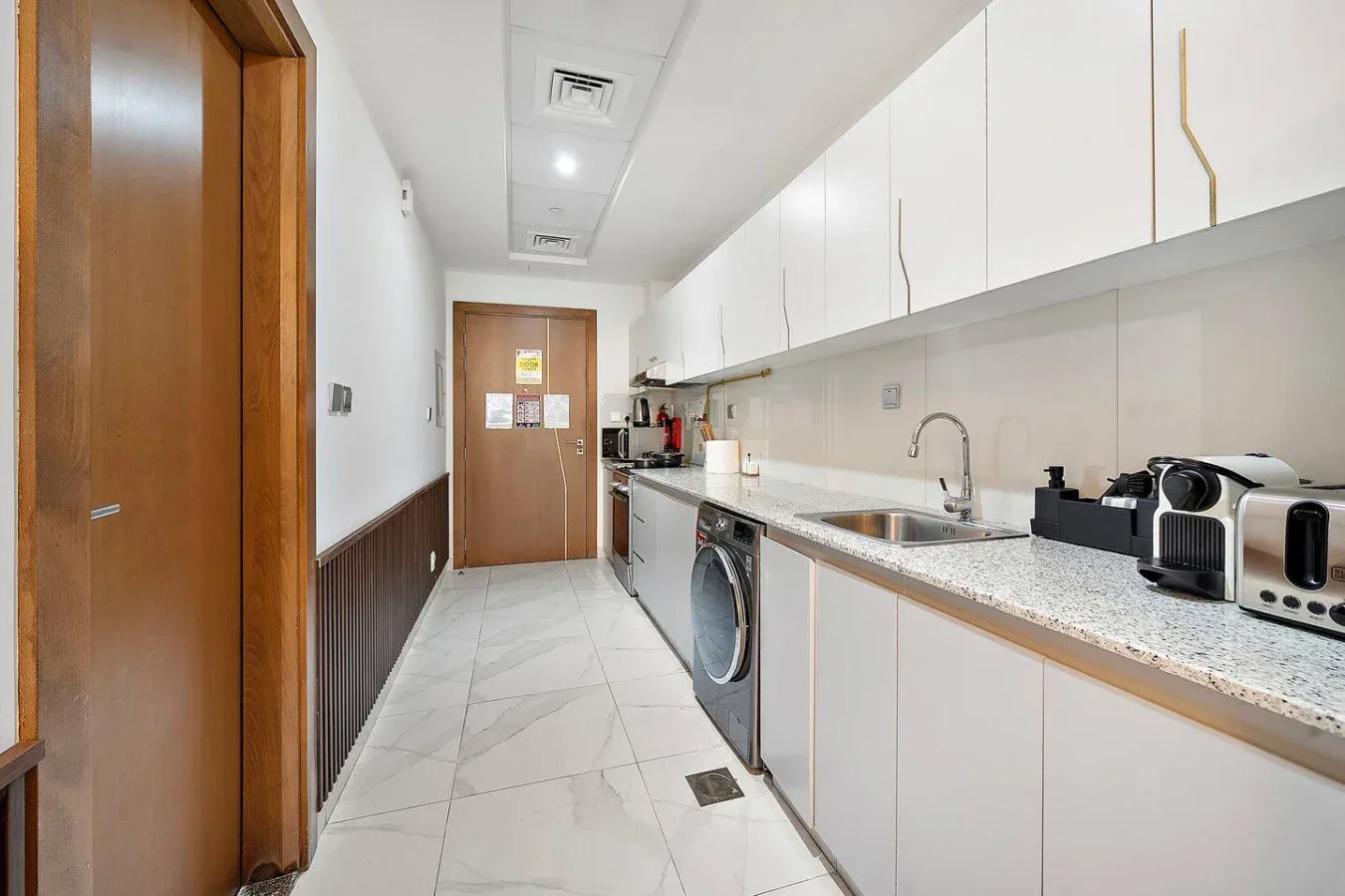 Una cocina alargada y luminosa con gabinetes blancos y una encimera extensa.