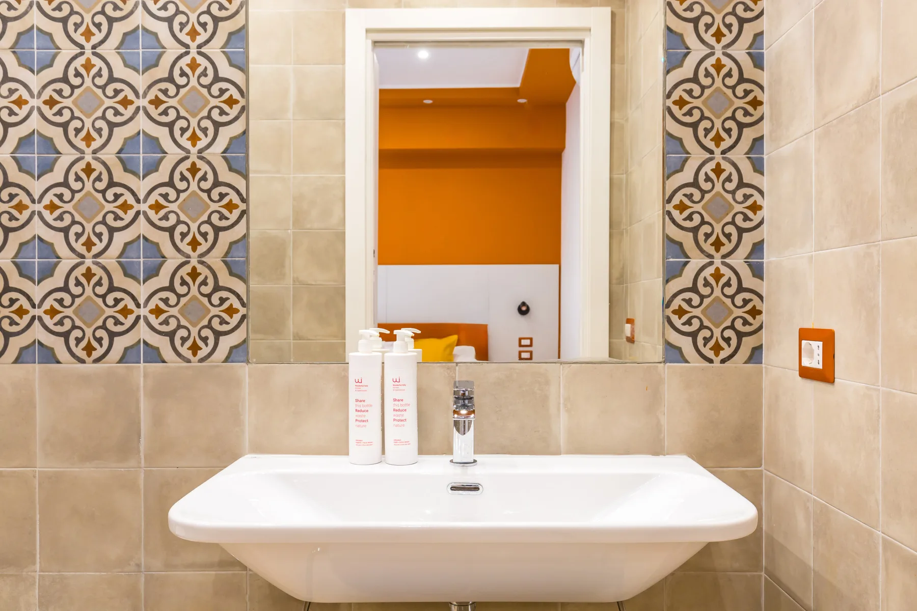 A tiled bathroom vanity with a white sink beneath a patterned mirror.